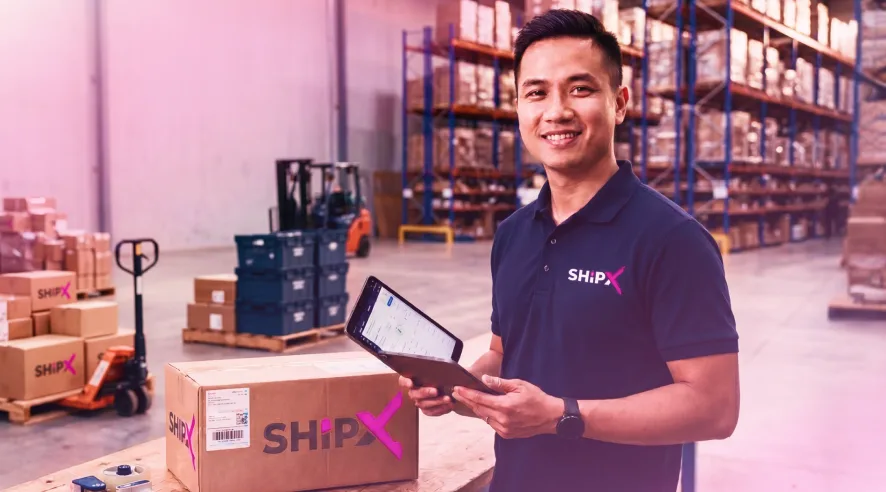 Nhân viên ShipX trong kho hàng cầm máy tính bảng bên cạnh các kiện hàng thương hiệu ShipX